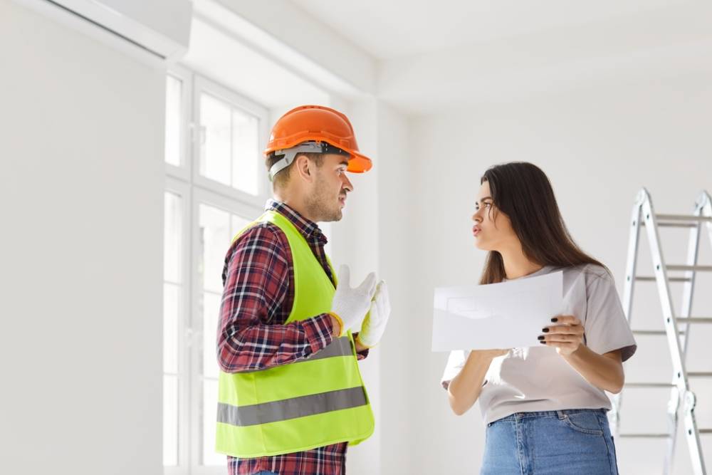 Displeased client and worker argue while discussing a blueprint and renovation project estimate for a home