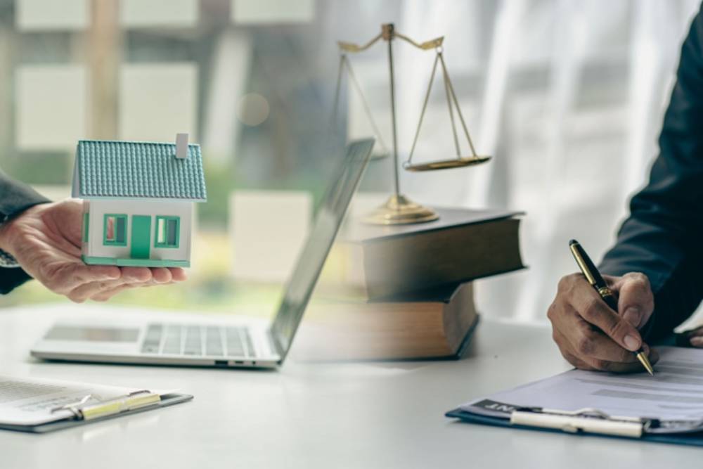 Judge holding wooden judge hammer against house background and businessman documents and house model on wooden table Real estate disputes